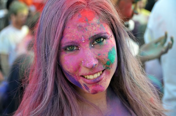 HoliMadrid 2015: Bollywood en la Gran Vía de Madrid. Primer plano de una chica rubia pintada con colores y con brillantes en el lagrimal, en la frente