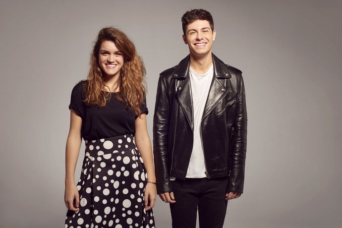 Alfred y Amaia muy divertidos, ella con una camiseta negra básica y una falda negra de topos en blanco con vuelo y el pelo suelto y ondas surferas y él con camiseta blanca, chaqueta de cuero y pantalón