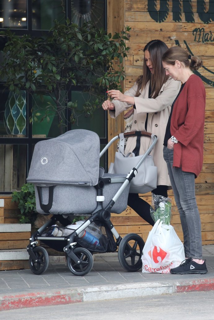 Eva González todo arte con su hijo Cayetano, le sale la vena andaluza y se pone a tocarle los pitos a su hijo en plena calle mientras él está en el carrito. Eva lleva una trench en color camel y un jersey y leggun en negro y unos botines de cuña de esparto ideales.