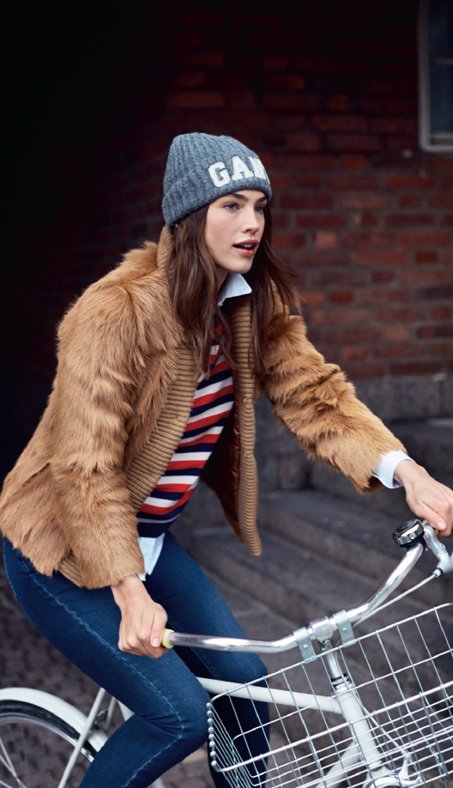 Chica vestida de gant con jersey marinero de rayas rojas y azules horizontales, vaqueros, chaleco y gorro con pompón 