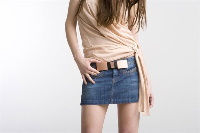 Chica con camisa en color nude y minifalda vaquera con un cinturón kemwek en negro y chapas metálicas en dorado mate