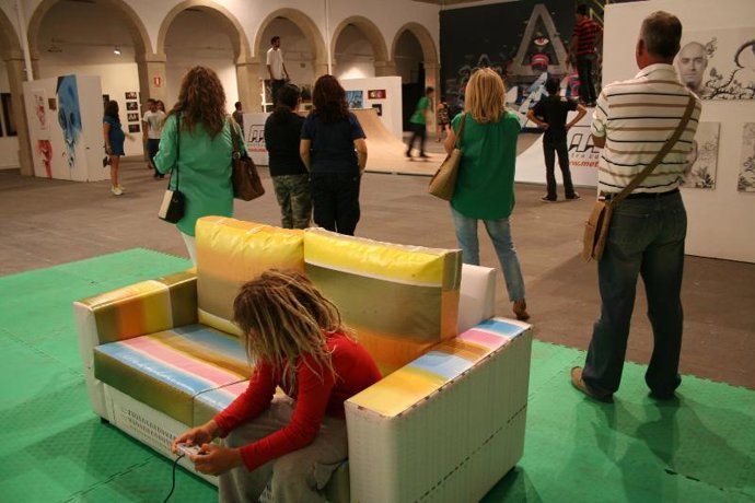 Un niño juega a la videconsola mientras el público ve la exposición del 'Plátano