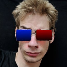 A young white Caucasian adult teenager wears real 3D glasses with metal rims.