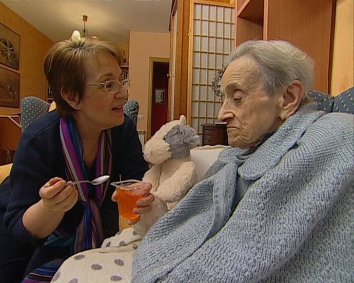Una cuidadora da de comer a una anciana