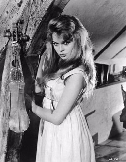 1957:  French actress Brigitte Bardot poses next to a string instrument in a pro