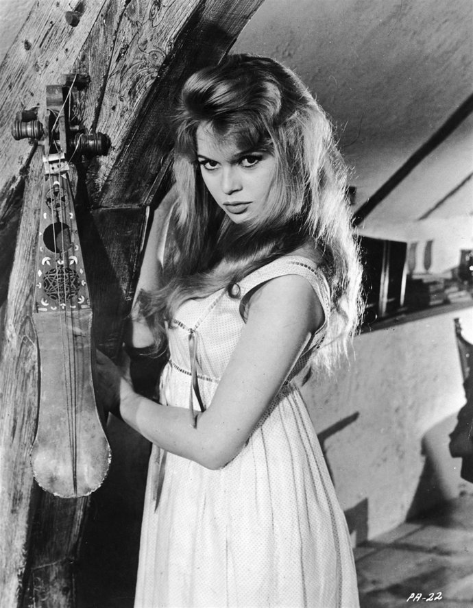1957:  French actress Brigitte Bardot poses next to a string instrument in a pro
