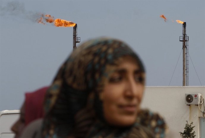 Una mujer camina frente a las torres petroleras de Libia