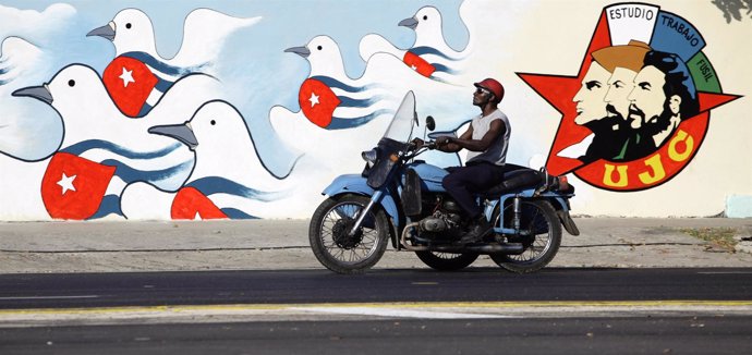 Cuba. A Man Rides His Motorcycle Past A Freshly Painted Mural