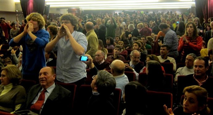 Dos manifestantes corean consignas, mientras el fondo de la sala protesta
