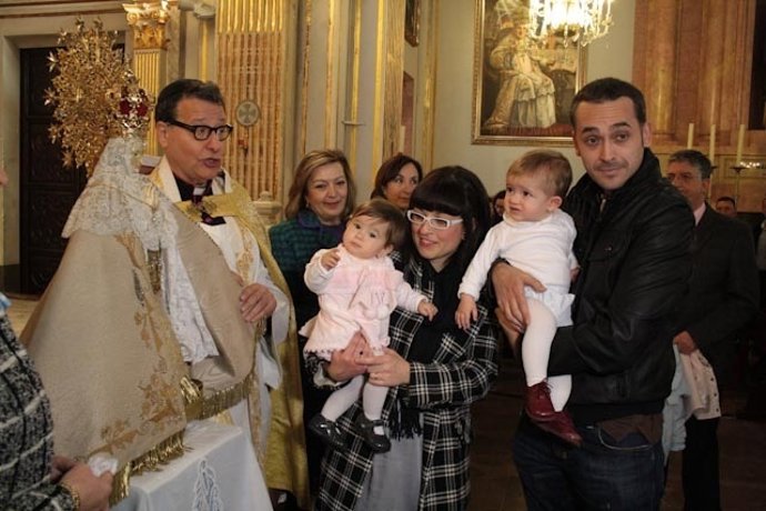 Una familia pasa a sus pequeños por el manto de la Virgen del Lledó
