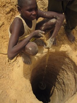 Niño Busca Agua En Un Pozo Medio Seco En Chad. Crisis Alimentaria. Hambruna.