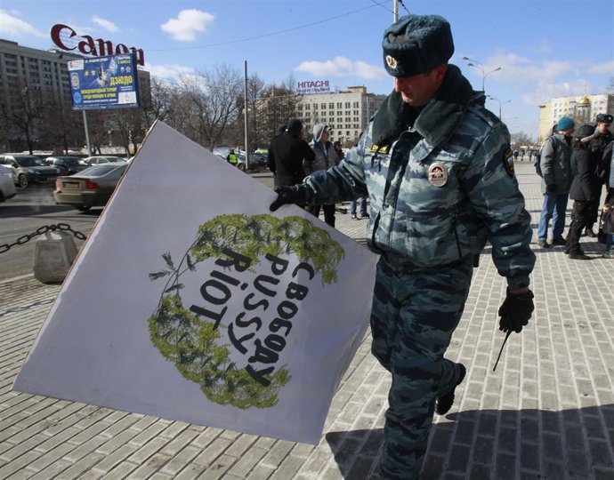 A Russian police officer removes a placard during a protest calling for the rele