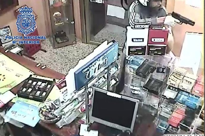 Uno de los atracadores empuña un arma de fuego en el estanco