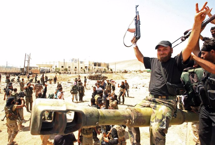 Un combatiente del Ejército de Liberación Sirio celebra, sentado sobre un tanque