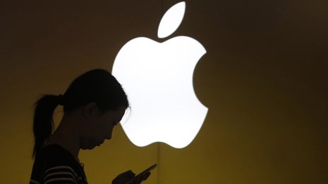 Una mujer mira la pantalla de su teléfono al frente de un logo de Apple fuera de