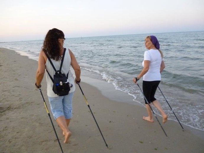 Dos personas realizan 'Nordic Walking' en una playa onubense