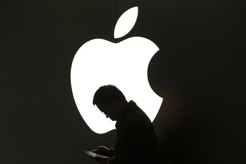 Un hombre revisa su iPad frente a un logo de Apple en las afueras de una tienda 