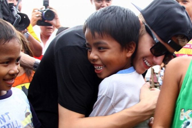 Canadian pop megastar Justin Bieber (C, black shirt) hugs a young survivor of Su