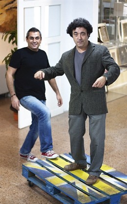 Nacho y Alecs sobre una mesa-palé-bandera entre canaria y del Reino Unido