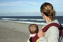 Mujer con bebé en portabebés mirando el mar
