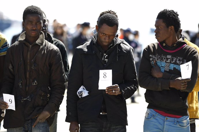 Migrants hold their identification numbers as they arrive at the Sicilian port o