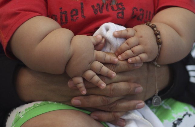 Un bebé obeso agarra las manos de su madre