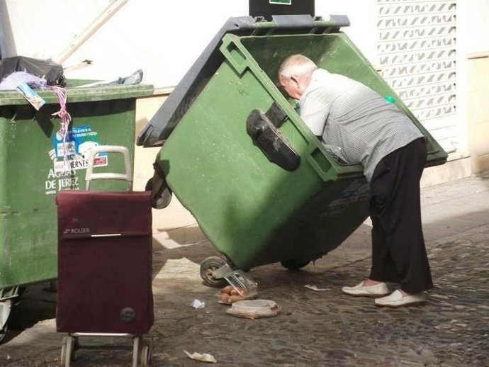 Un mendigo busca comida en un contenedor