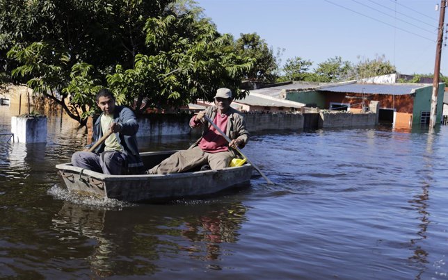 Men travel on a boat near flood-affected houses in Asuncion