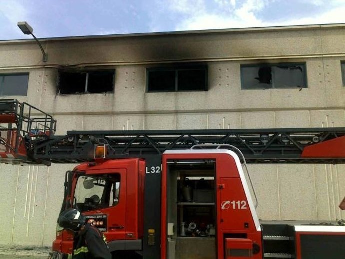 Un bombero y el vehículo escala delante de la nave afectada por el incendio
