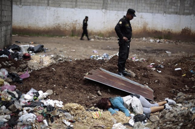 Police officers stand near the dead body of a woman in a garbage dumping ground 