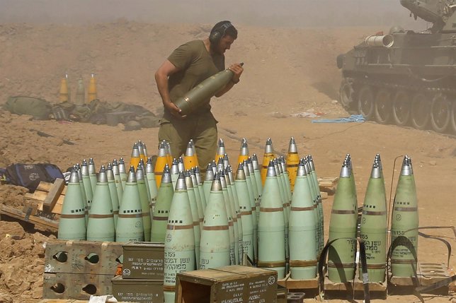 An Israeli soldier carries a shell at a mobile artillery unit while it fires