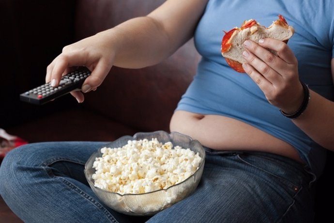 Mujer sedentaria comiendo y viendo la televisión