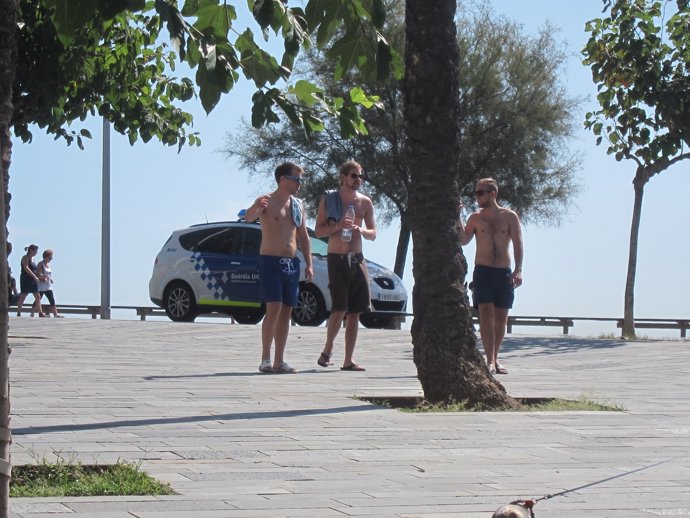 Turistas sin camiseta ante un coche de la Guardia Urbana en la Barceloneta