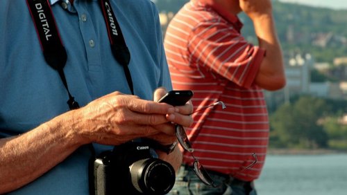 Turista en la playa con cámara y teléfono móvil smartphone verano vacaciones
