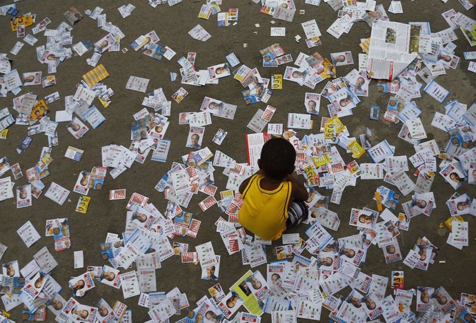 Niño juega con octavillas electorales frente a un colegio electoral