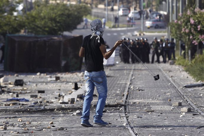 Palestino con una honda ante policías israelíes en Jerusalén