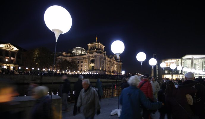 People walk under the lit balloons installation along the river Spree in front o