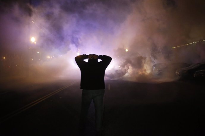 A protester stands with his hands on his head as a cloud of tear gas approaches 