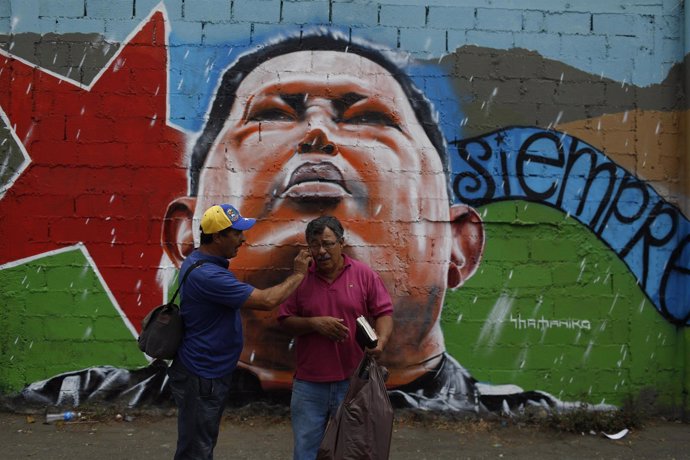 Hombres hablando tras la imagen de Hugo Chávez en Venezuela