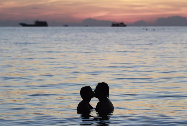 A couple kisses during sunset by the island of Koh Tao