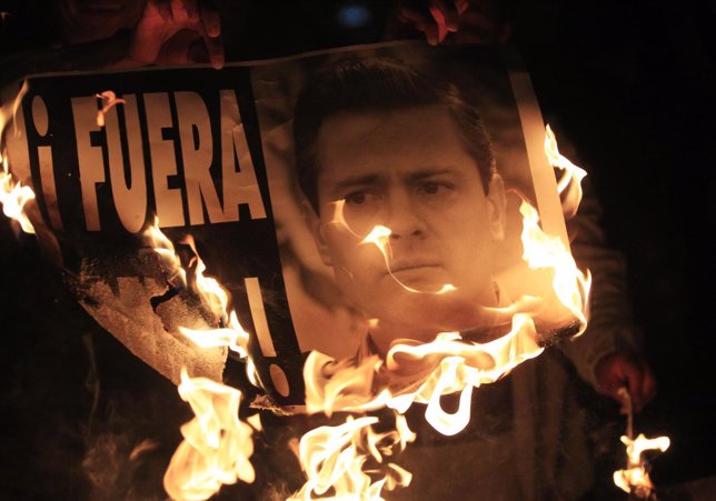 Demonstrators burn a sign with a photograph of Mexico's President Enrique Pena N