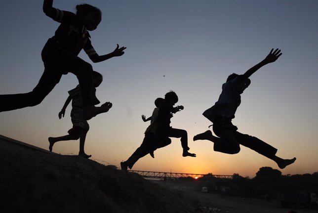 Children play on a sand dune as they are silhouetted against the setting sun in 