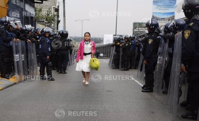 Girl walks past riot policemen guarding one of the access roads to Benito Juarez
