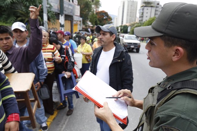 A Venezuelan soldier controls the crowd as people wait to shop for electronic go