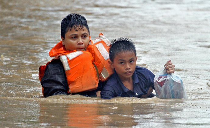 Una policía ayuda a un niño en inundaciones en Filipinas