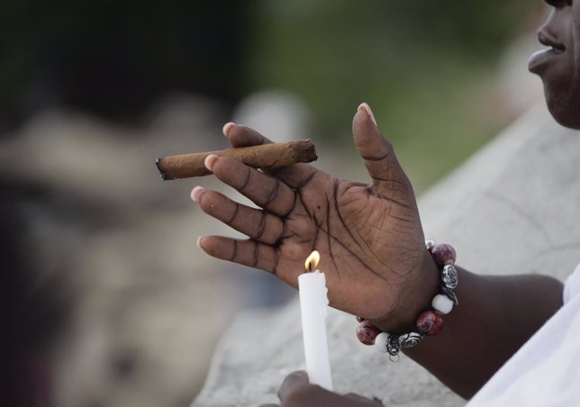 A woman prays as she holds a cigar and a candle on the shores of Regla, a distri