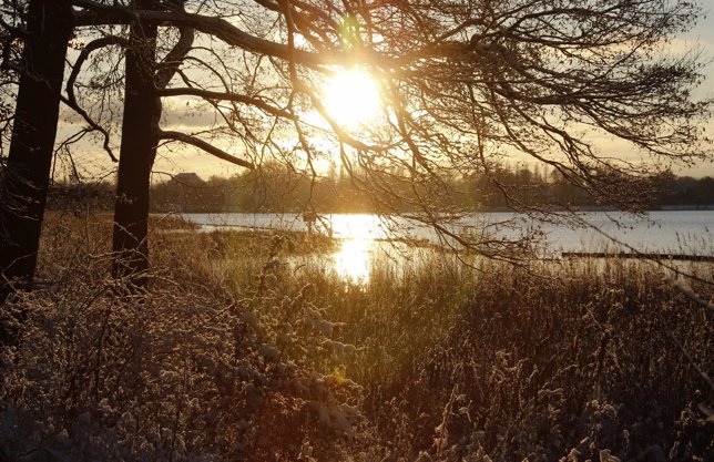 The sun sets over Havel river at the snow-covered Glienicke Palace forest after 