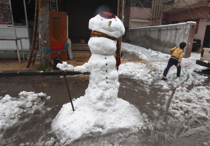 Un niño junto a un muñeco de nieve en Damasco