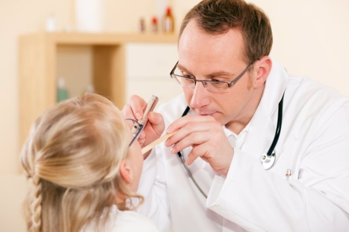 Un pediatra le examina la gargantra a una niña con tos.