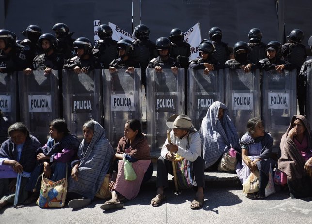 Indigenous people sit during a protest with others, in front of riot police, out